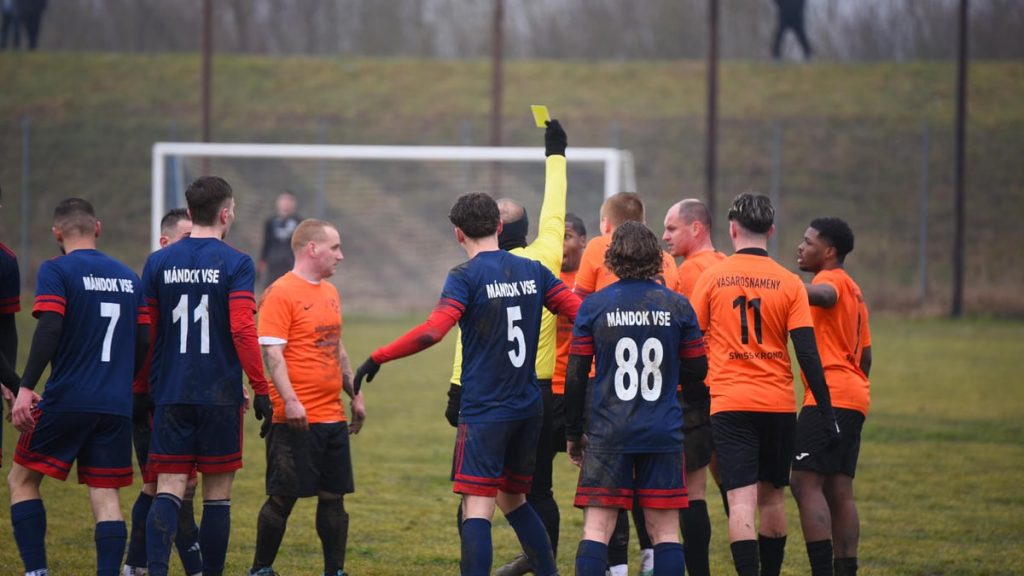 Soccer players show sportsmanship as referee issues yellow card during a match in Vásárosnamény, Hungary.